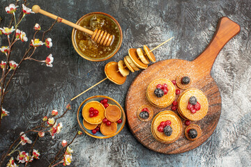 Top view of American pancakes on cutting board and honey with spoon on gray table