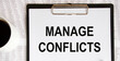 © Veranika - ON the letter tablet, the text is MANAGE CONFLICTS, next to a coffee mug, reports.