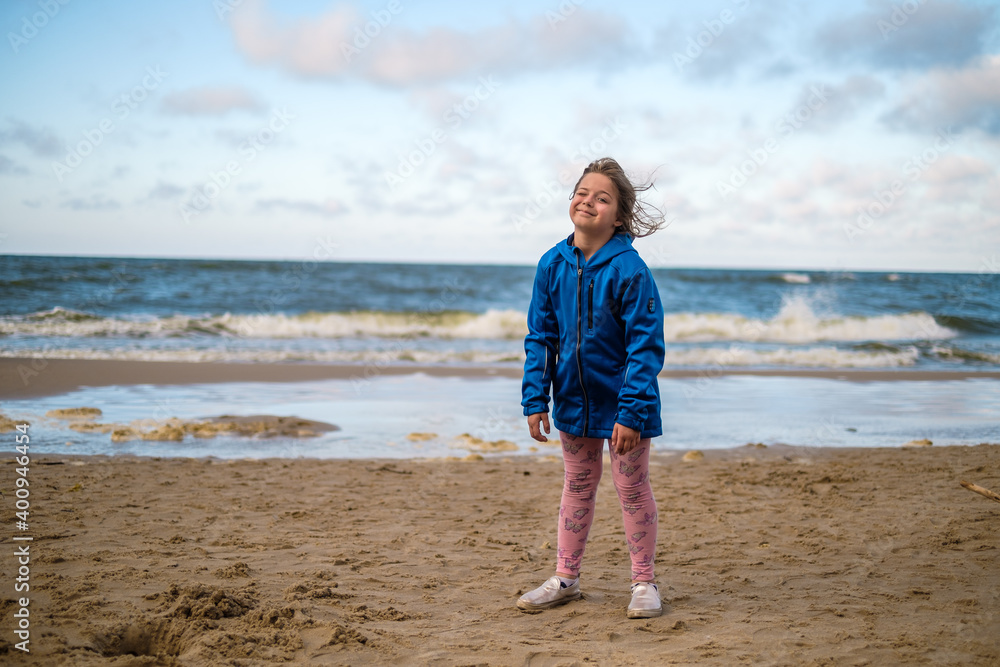 Dziewczynka w niebieskiej kurtce stojąca na plaży nad morzem - obrazy, fototapety, plakaty 
