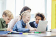 © Comeback Images - Group of elementary students enjoying computer science class given by female teacher sitting at desk in classroom