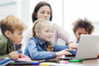 © Comeback Images - Female teacher explaining computer science to group of diverse elementary students looking at laptop screen sitting at desk in classroom