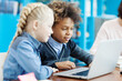 © Comeback Images - Two elementary school kids, mixed race boy and Caucasian girl, studying on laptop computer sitting at desk in classroom