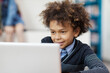 Mixed race curly-haired schoolboy browsing Internet on laptop computer in classroom and smiling