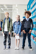 © Comeback Images - Full length portrait of diverse group of three elementary students looking at camera standing by book shelves in school library