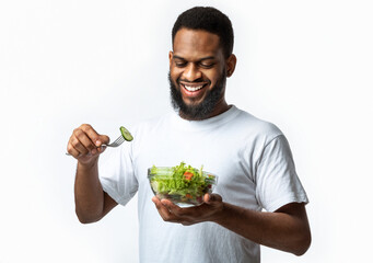 Wall Mural - Happy Black Man Eats Fresh Vegetable Salad Over White Background