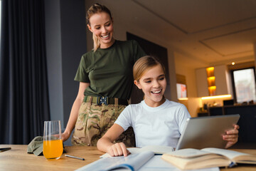 Wall Mural - Beautiful happy military woman doing homework with her daughter at home