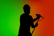 © master1305 - Move. Silhouette of young male guitarist isolated on green-orange gradient studio background in neon. Beautiful shadow in action, performing. Concept of human emotions, expression, ad, music, art.