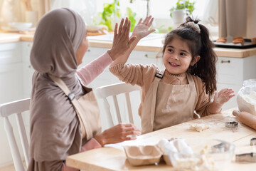 Wall Mural - Happy Muslim Mom And Daughter Giving High-Five To Each Other In Kitchen