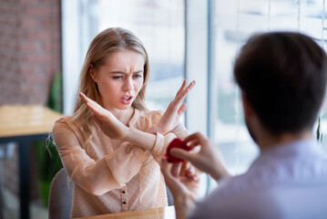 Scared young woman rejecting marriage proposal, gesturing NO, refusing to accept engagement ring at cafe