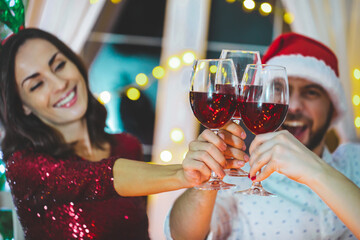 Group of cheerful young friends celebrating Christmas together at home having fun and drinking red wine