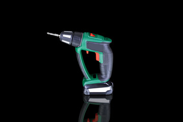 Portable electric screwdriver on black background on reflective surface, side view. Green device with red buttons.