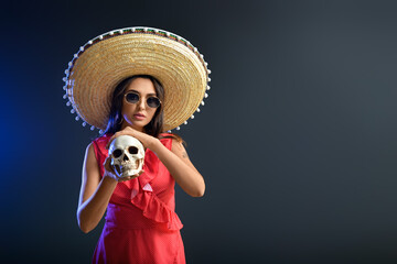 Beautiful young woman in sombrero hat and with skull on dark background. Celebration of Mexico's Day of the Dead