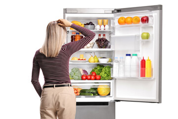 Canvas Print - Rear view of a woman standing in front of an open fridge with vaiety of food