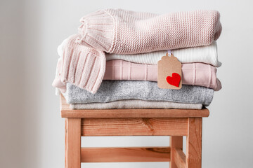 Pile of warm knitted pullovers in pastel colors with label decorated by heart