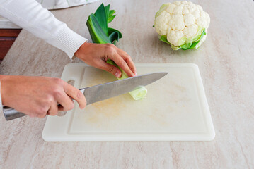 Woman cutting leek with steel knife on plastic cutting board