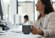 © Paul Bradbury/Caia Image - Businesswoman drinking coffee at computer in office
