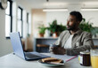 © Paul Bradbury/Caia Image - Thoughtful businessman drinking coffee at laptop in office