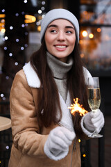 Wall Mural - Happy young woman with sparkler and glass of champagne at winter fair