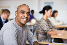 Portrait Of Focused Young Adult Male Studying In Classroom With Colleagues