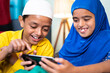 © WESTOCK - Two muslim sibling kids busy using mobile at home - concept of kids using technology, internet and social media.