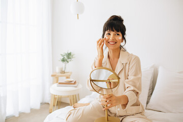 Wall Mural - young woman doing makeup sitting on bed