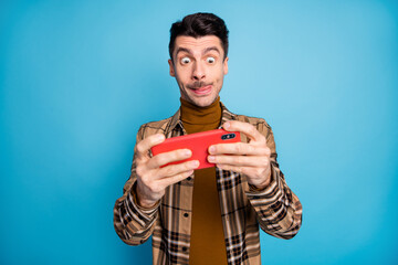 Photo of young funky funny focused addicted man playing video game in cellphone isolated on blue color background