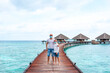 © klavdiyav - family father young man and his son wearing a protective face mask and stand on a pier near water villas in the Maldives, a concept of  travel during the covid pandemic