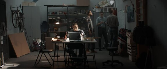 WIDE Group of young people discussing something, brainstorming. Launching their small IT business startup company from garage. Shot with 2x anamorphic lens
