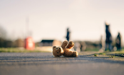 Wall Mural - Lost Teddy bear with sad face lying on footpath with blurry people ,Lonely bear doll laying down on the brick floor in gloomy day, Lost toy or Loneliness concept, International missing Children