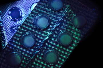 Fototapete - Pills or drugs in a package under neon light on a dark background pattern for design..