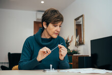 Senior Woman Sitting At Home, Studying The Instructions For A Self Test For COVID-19 With Antigen Kit On Hand. Holds A Nasal Swab For Possible Infection Of Coronavirus. Health Services Online.