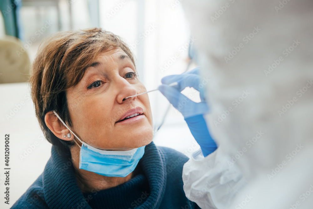 Close up of the face of senior female patient being tested for Covid-19 with a nasal swab, by a health Professional protected with gloves and PPE suit. Rapid Antigen Test during Coronavirus Pandemic. - obrazy, fototapety, plakaty 