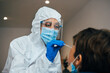 © BASILICOSTUDIO STOCK - Close up of female health Professional in PPE introducing a nasal swab to a senior female patient at her house. Rapid Antigen Test kit to analyze nasal culture sampling while coronavirus Pandemic.