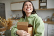 © Anatoliy Karlyuk - Cheerful teenage girl expressing positive emotions receiving unexpected birthday gift holding parcel and smiling with pleasure. Dark haired young woman posing with cardboard box with new cosmetics