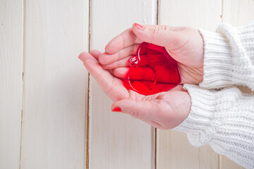 Female hands hold a glass red heart. Valentine's day greeting card. Care and health concept, healthcare, heart health theme top view copy space