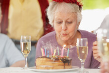 Senior Woman Blowing Out The Candles On A Birthday Cake