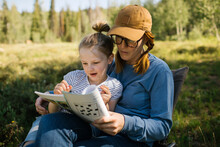 USA, Utah, Uinta National Park, Mother And Daughter (6-7) Doing Crossword In Meadow In Forest