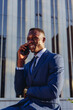 © David Espejo/ADDICTIVE STOCK - Low angle of happy successful well dressed black male manager in classy suit answering phone call while sitting against contemporary city building