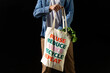 © David Munoz/ADDICTIVE STOCK - Crop anonymous male buyer holding fabric shopping bag with text message of reuse and recycle concept on black background