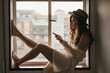 © Gustavo Pozo/ADDICTIVE STOCK - Young sensual female in trendy outfit and straw hat text messaging on cellphone while sitting on windowsill