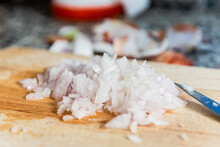 Closeup Of Chopped Onion On Wooden Cutting Board With Knife Placed On Kitchen Table During Cooking Process