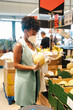 © Jake Jakab/ADDICTIVE STOCK - Side view of African American female customer in protective mask and gloves picking ripe watermelon from box while making purchases in supermarket during coronavirus pandemic