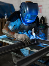 Unrecognizable Male Welder Using Welding Machine On Metal Detail While Working At Workbench In Factory