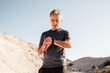 © Nico Mortarini/ADDICTIVE STOCK - Concentrated middle aged male athlete in activewear checking time on smartwatch while standing in hilly terrain after workout