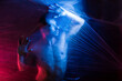 © Victor Prieto/ADDICTIVE STOCK - Pensive young handsome shirtless muscular male looking away while putting hands on surface of big transparent tape in light of blue and red lamps
