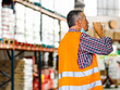 © Alberto Morcillo/ADDICTIVE STOCK - Side view adult male worker in orange high visibility vest and lowered mask drinking water from plastic bottle while standing near shelves in warehouse