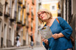 © Si And Si/ADDICTIVE STOCK - Low angle of female traveler holding touristic map and checking route while standing on narrow paved street with old buildings in Cuenca town in Spain
