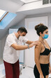 © Alvaro Montero/ADDICTIVE STOCK - Side view of focused male physiotherapist examining back of female patient wearing medical mask while standing in bright room