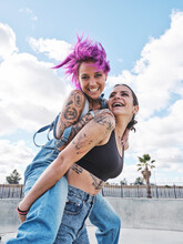 Low Angle Of Delighted Woman With Pink Hair Piggybacking Cheerful Female Friend With Tattoos While Having Fun Together At Weekend