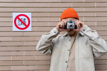 Carefree Male Taking Photos On Camera While Standing Against Wall With Restriction Sign Prohibiting Photography